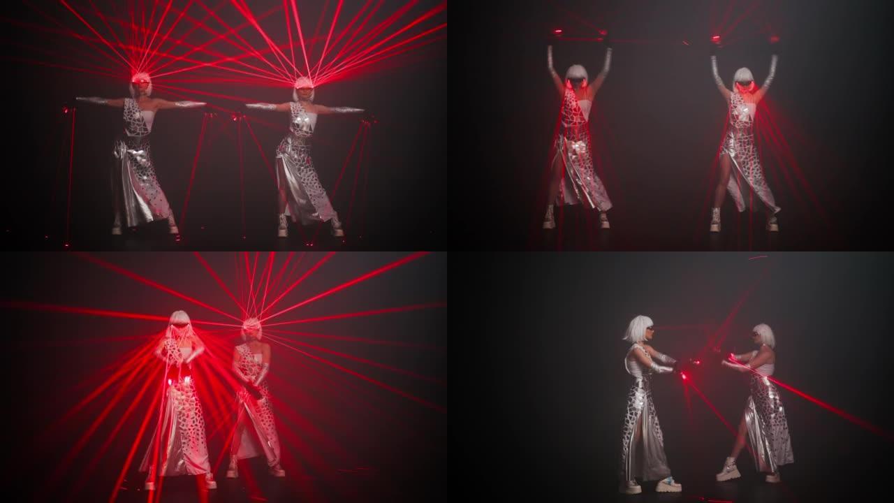 穿着红色霓虹灯在黑色背景下跳舞的服装中，自信的女表演者同时移动。苗条的专业高加索舞者用激光束在舞台上