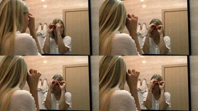 衰老。皮肤松弛。一名年轻女子通过照镜子做整容运动。面部建筑。现代护理，放松面部肌肉。整容，整形手术