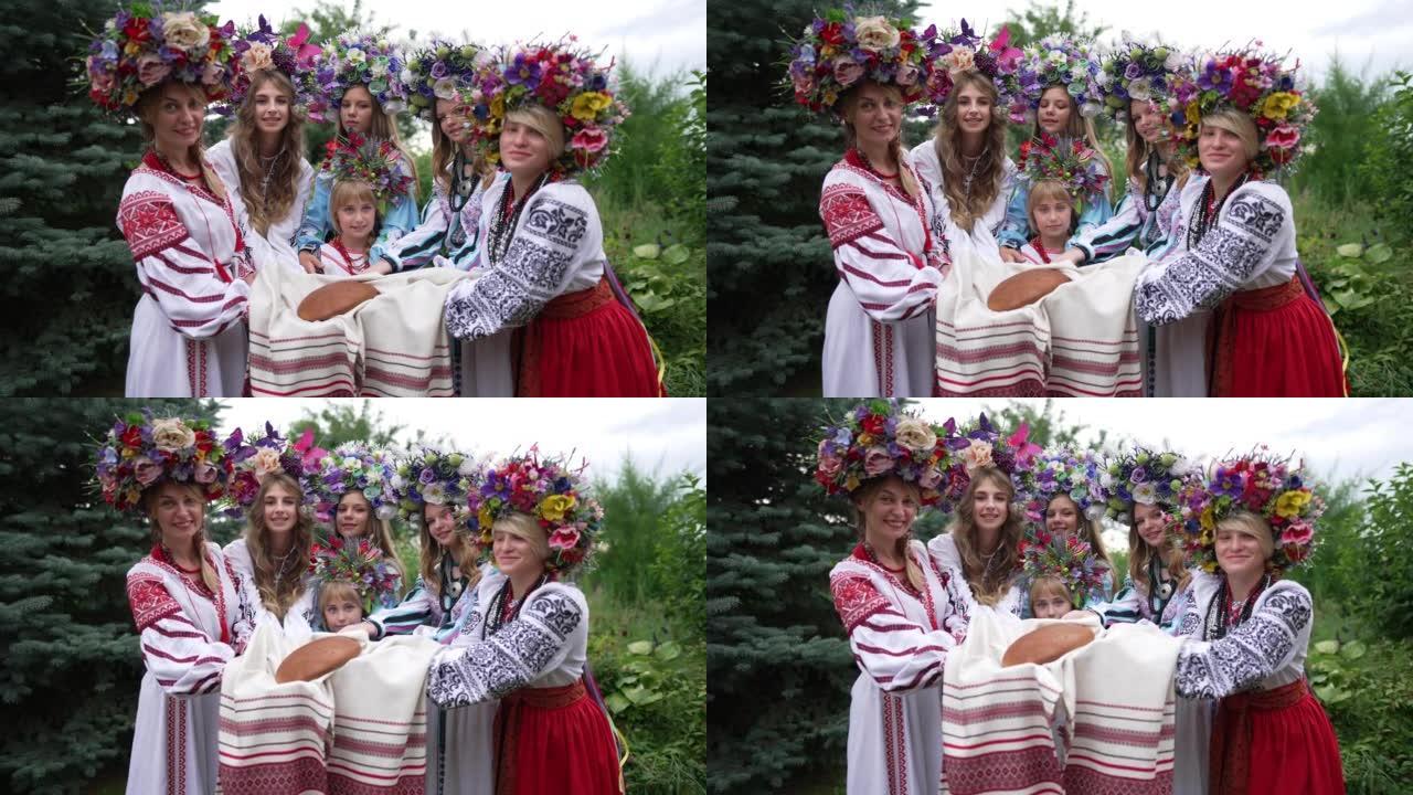 华丽的乌克兰年轻女性和可爱的小女孩在毛巾上伸展面包，看着相机微笑。一群积极迷人的女士在春天公园摆花圈