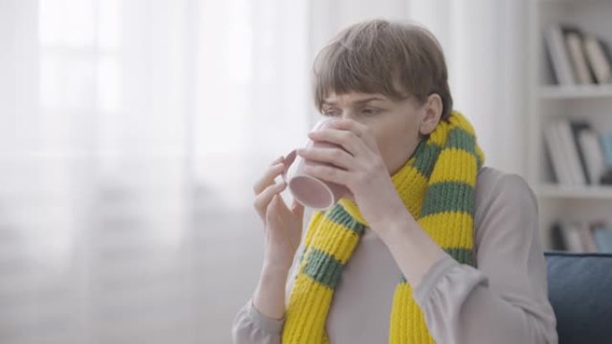 生病的女人咳嗽和喝热茶，戴着温暖的围巾，喉咙痛