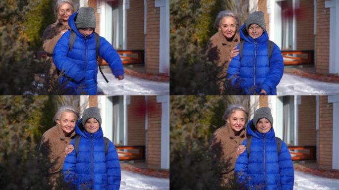 积极微笑的成熟女人帮助男孩穿上背包，看着相机微笑。冬日在后院，快乐自信的高加索母子在阳光下摆姿势的肖