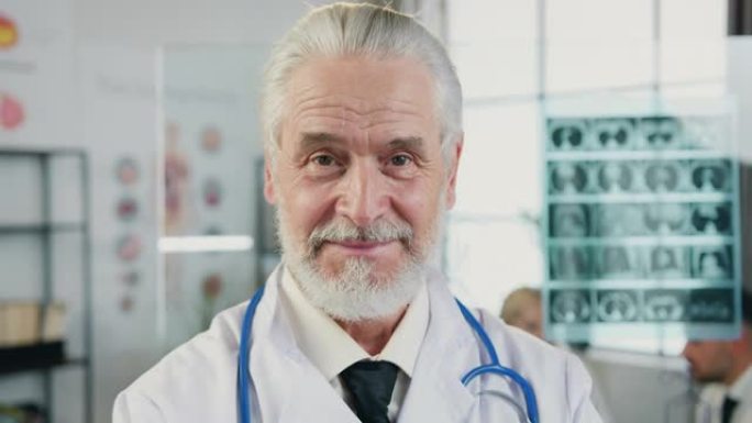 在医院的工作室里，面观积极的经验丰富的受人尊敬的白发大胡子医生的特写肖像，他们真诚地微笑着看着镜头