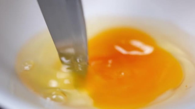 近距离刀以慢动作敲打蛋清和蛋黄。厨房白碗中鸡蛋部分混合的过程。