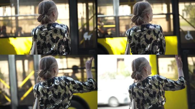 后视图开朗的年轻白人妇女向黄色巴士挥手告别，传递空气之吻。快乐苗条美丽的女士站在公共交通站的人行道上