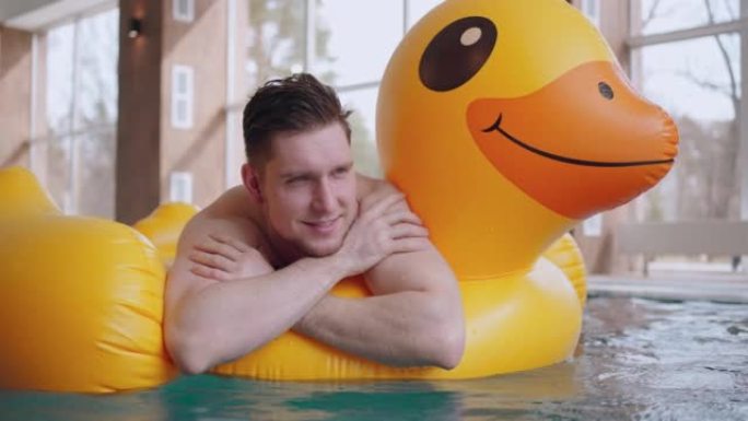游泳池或热水浴的快乐男性游客漂浮在充气鸭上，肖像