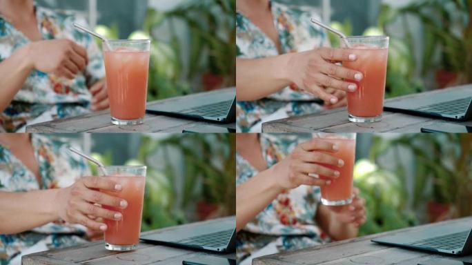 一个女人在使用latop时拿起果味饮料的细节镜头