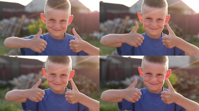 兴奋的男孩竖起大拇指看着相机，在户外微笑。快乐开朗的孩子在彩色背景下摆姿势的肖像。快乐的小男孩发出积