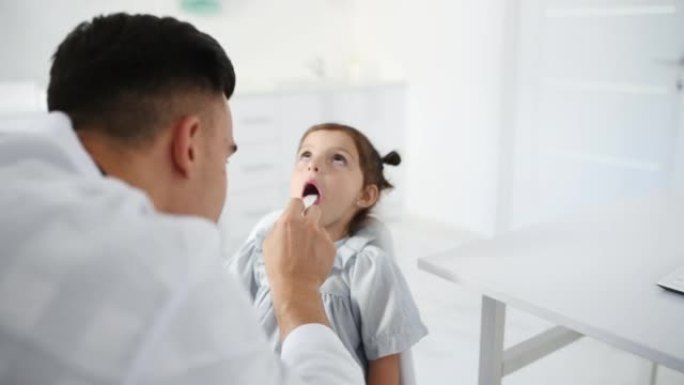 穿着白大褂的年轻医生用医用扁桃体咀嚼小女孩的喉咙