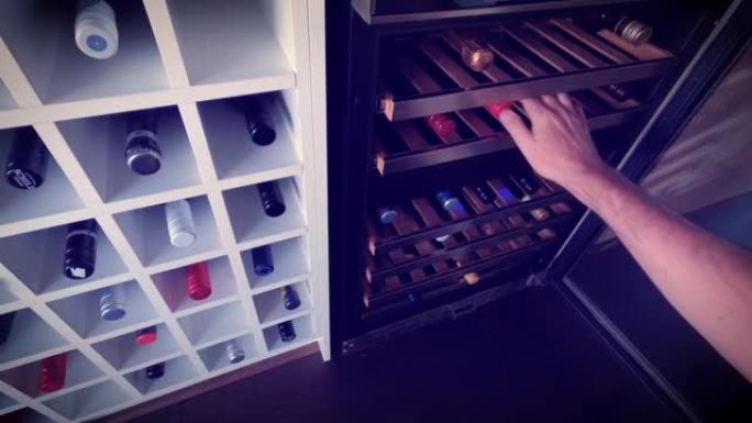 一名男子打开葡萄酒冰箱为架子选择冰瓶的慢动作。特写。