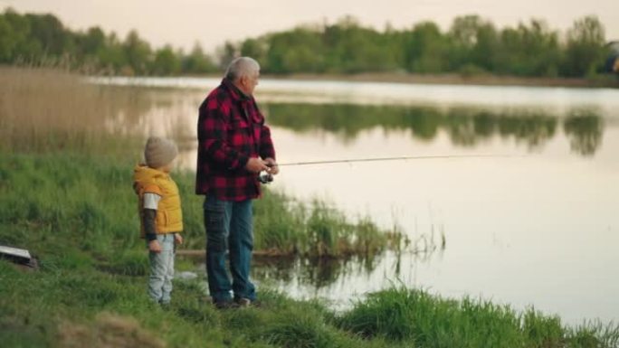老人和他的孙子早上在美丽的湖岸一起钓鱼