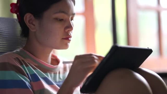 亚洲妇女坐在符合人体工程学的椅子和数字笔在平板电脑上画画。