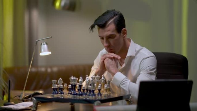 集中的棋手坐在家里练习。专注的中东男子在室内提高技能的肖像。爱好和生活方式概念。
