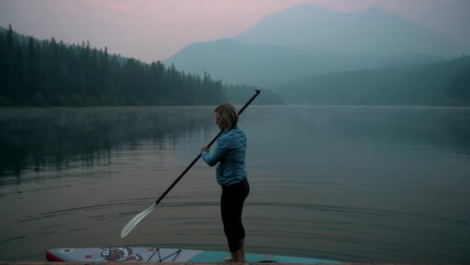 女人站在烟熏湖对面的桨板 (sup)