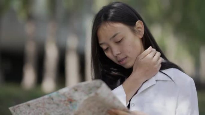 年轻快乐的亚洲女性，纸质地图站在公园小巷选择方向。轻松自信迷人的女性游客户外搜索路线微笑的肖像。旅行