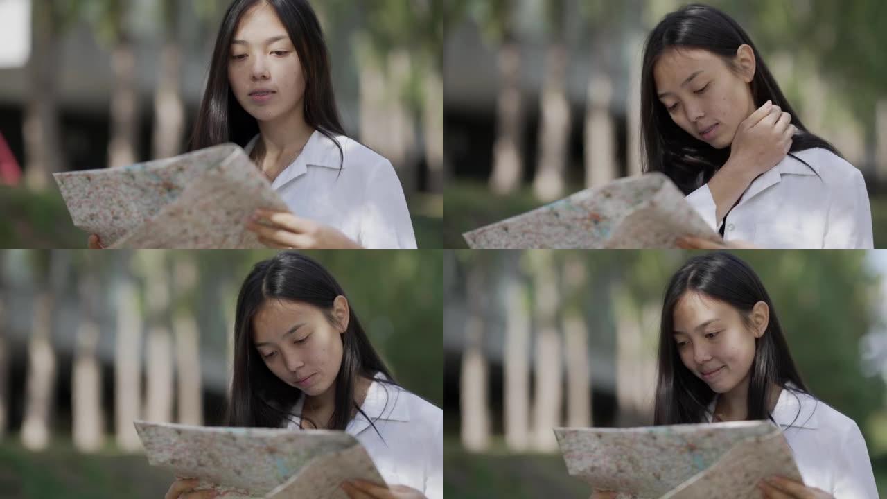 年轻快乐的亚洲女性，纸质地图站在公园小巷选择方向。轻松自信迷人的女性游客户外搜索路线微笑的肖像。旅行