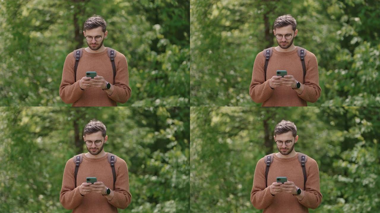 一名男子在手机上的树林里背着背包，正在网上寻找信息，阅读新闻，预订。自然界中的游客查看内容，通过GP