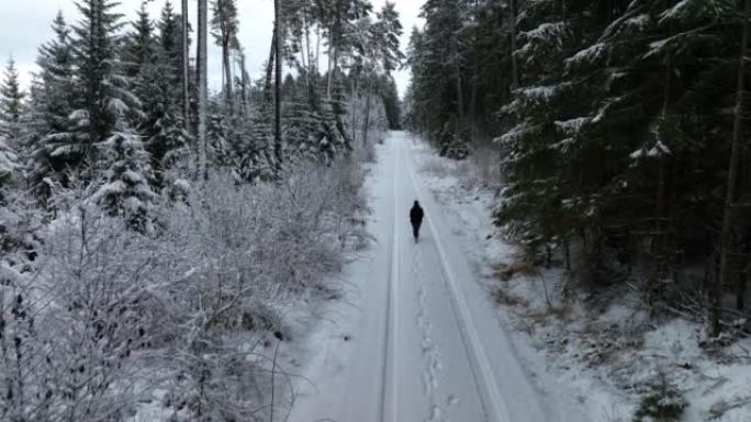 空中无人机拍摄了一名妇女在树林中沿雪道行走的镜头