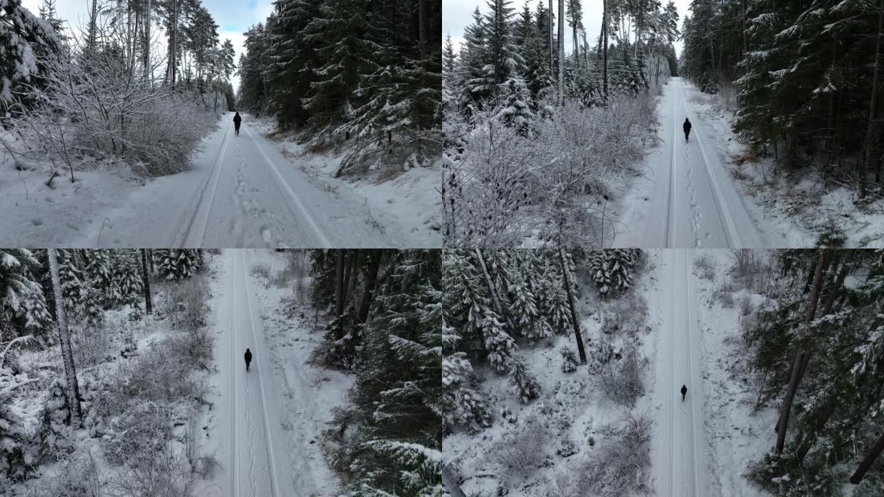 空中无人机拍摄了一名妇女在树林中沿雪道行走的镜头