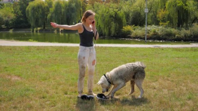 年轻女子带着她的白色大皮毛脏狗，因为城市公园湖里的绿色脏水
