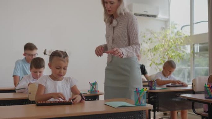 控制小学学习过程的女教师。一位女老师走在课桌之间，在完成任务后照看