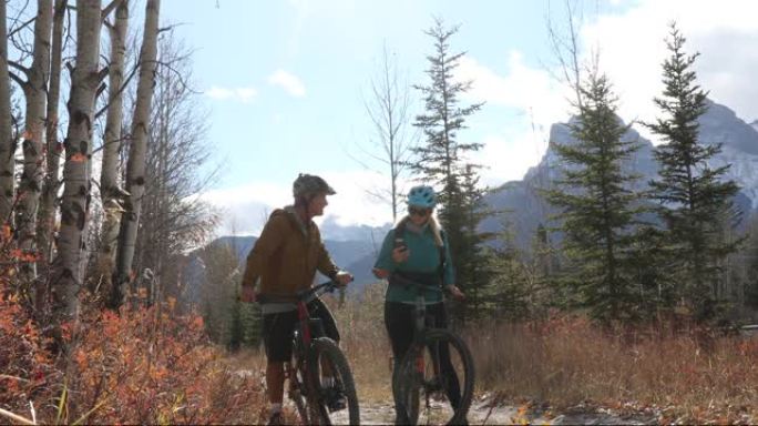 山地自行车夫妇在高山小径上停下来检查方向，远处的山脉