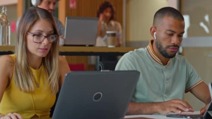 年轻的男人和女人坐在办公空间的办公桌前，在笔记本电脑上工作