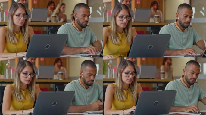 年轻的男人和女人坐在办公空间的办公桌前，在笔记本电脑上工作