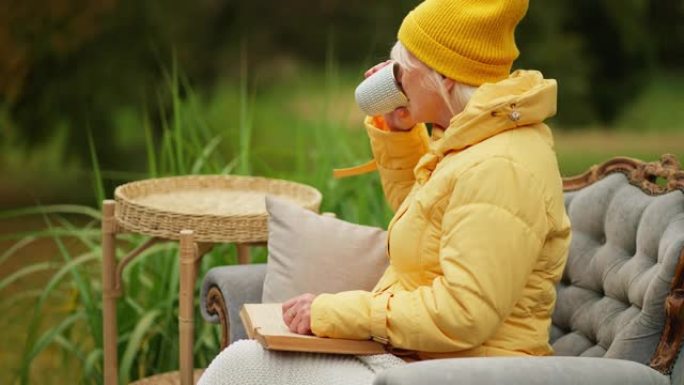 生病的老年妇女患者看书并在外面的椅子上使用手机并喝茶