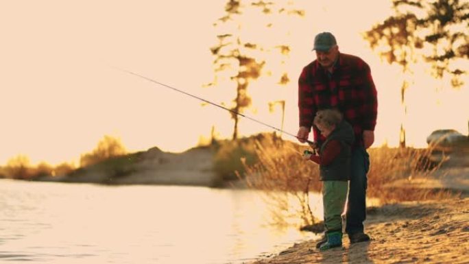 阳光明媚的傍晚，老渔夫和小男孩在河边或湖边钓鱼，幸福的家庭周末