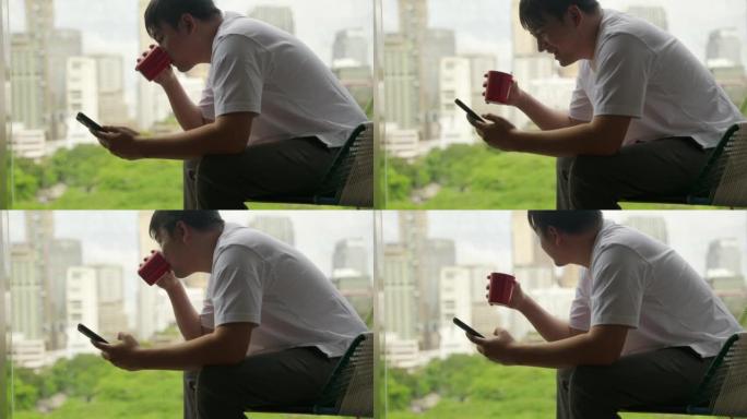 亚洲人坐在一栋享有城市美景的建筑的阳台上喝咖啡。