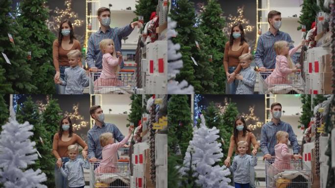 一个四口之家，父亲和孩子一起选择一棵圣诞树。商店里戴着医用口罩的幸福家庭以慢动作购买圣诞节装饰品和礼