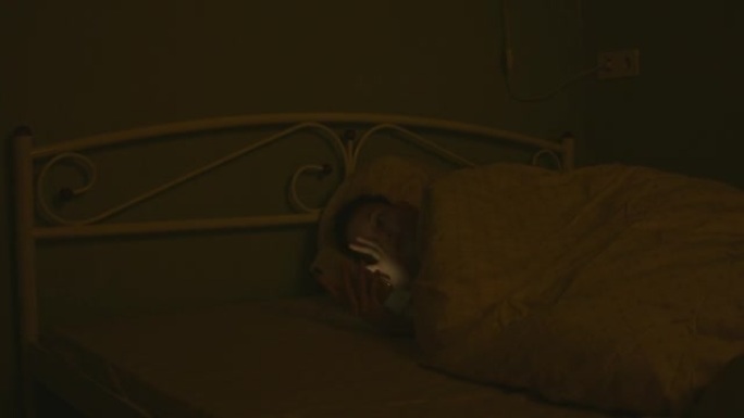 一名年轻女子放下智能手机，关掉灯，晚上睡在床上。