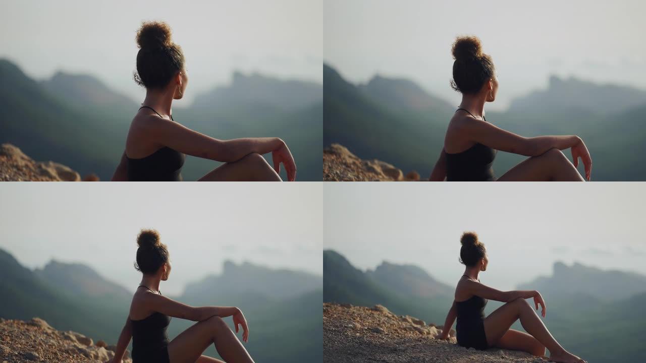 非洲族裔妇女在悬崖上放松，看着令人叹为观止的景色