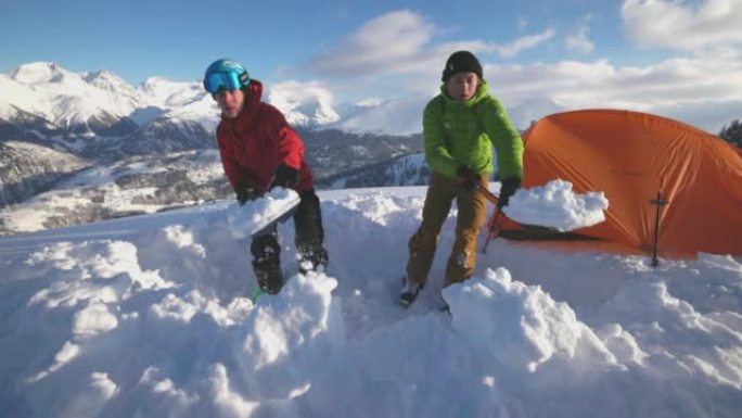 一对滑雪者在雪山上架起帐篷