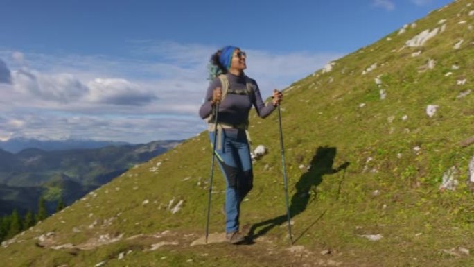 女徒步旅行者在阳光下的风景优美的小径上爬山