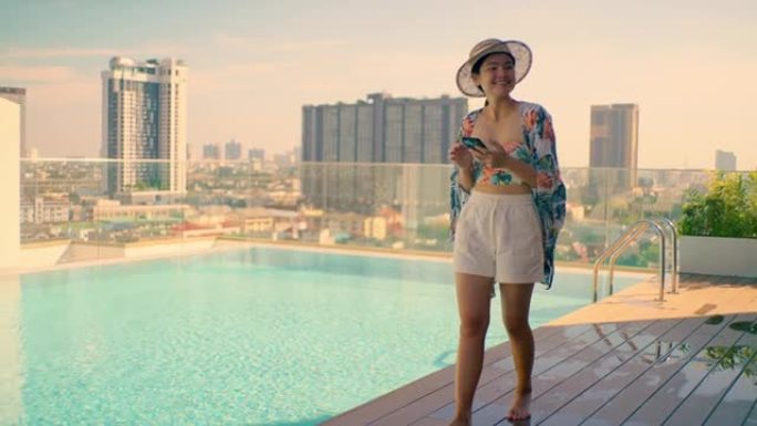 高层建筑上的亚洲女孩屋顶游泳池，并在手机中查看社交媒体。