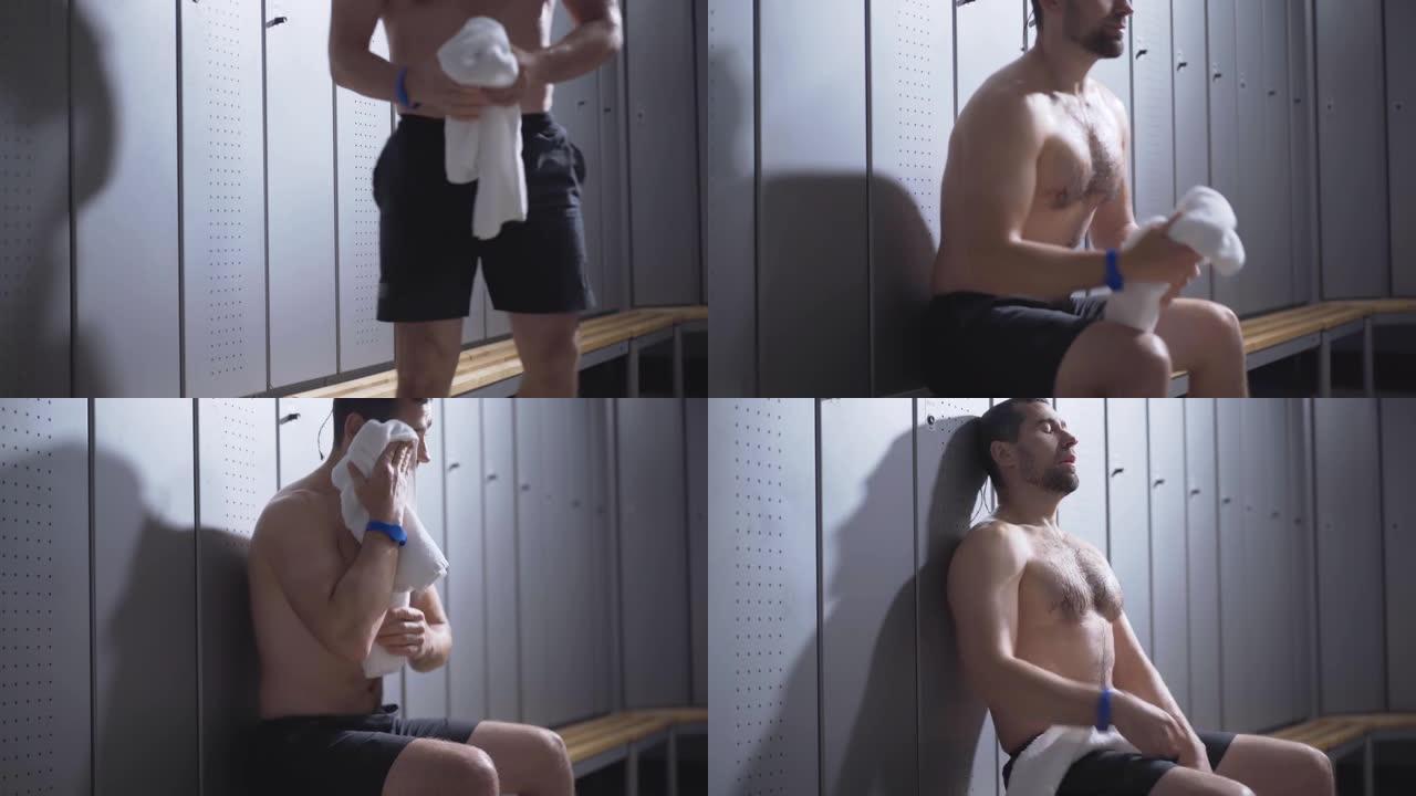 年轻英俊的白人运动员赤裸的躯干进入更衣室，坐下来用白毛巾擦脸。锻炼后，筋疲力尽的人靠在健身房的储物柜