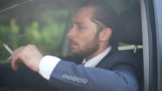 年轻的紧张男子坐在驾驶座上的阳光中抽烟。体贴陷入困境的高加索商人在车里的肖像。不健康的生活方式概念。