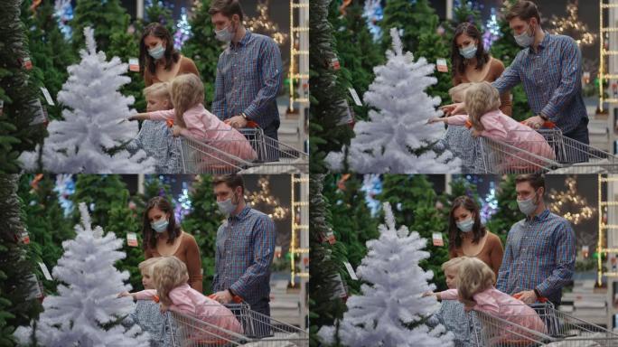 爸爸妈妈的女儿和儿子一起出去圣诞树。商店里戴着医用口罩的幸福家庭以慢动作购买圣诞节装饰品和礼物