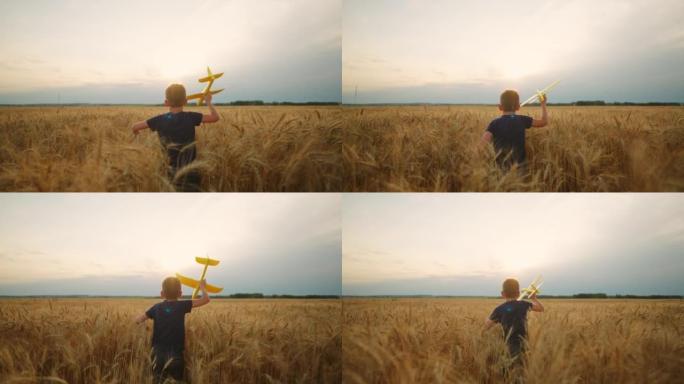 手里拿着玩具飞机的迷人小男孩在金色的黑麦球场上奔跑，在多云的天空中后视