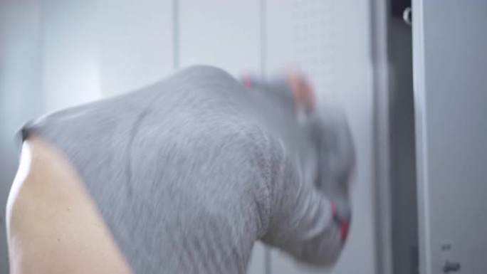 成年运动员在更衣室打开储物柜并脱衣服。训练前在健身房换的白人男子。健康生活方式和男性气质的概念。