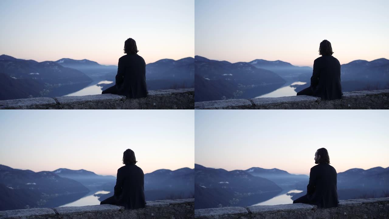 商人坐在日落时俯瞰山脉和湖泊的边缘
