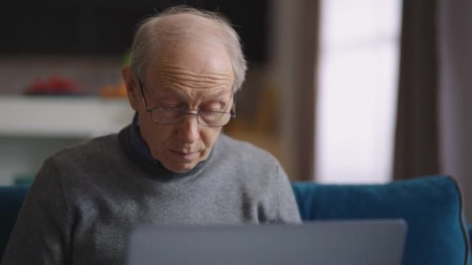 年老的严肃男人正在家里用笔记本电脑工作，公寓里的老人肖像，使用现代笔记本电脑