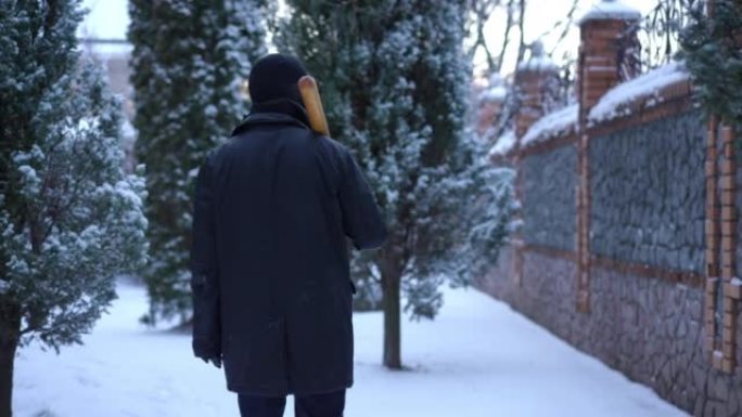 背景网窃贼与棒球棒走在户外白雪皑皑的后院。现场摄像机跟随自信的男子戴着滑雪面具漫步在白雪上环顾四周。