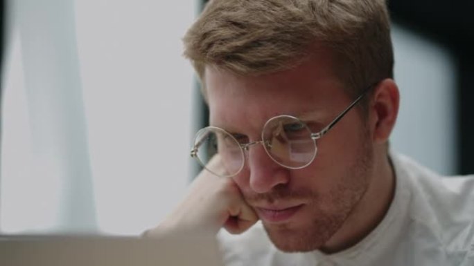 戴眼镜的聪明白人正在笔记本电脑屏幕上阅读信息，脸部特写视图
