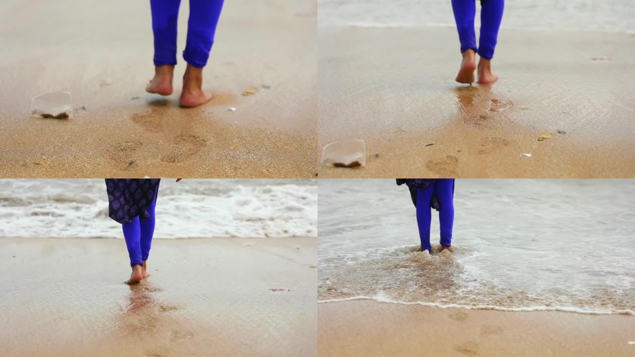 一个年轻女孩光着脚走路，留下脚印的特写镜头，抚摸着沙滩上溅起的水，海浪向她走来。