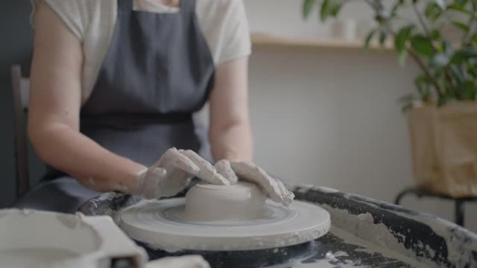 老年妇女大师在陶工的轮子上工作，并以慢动作在她的车间里制作了一杯陶瓷