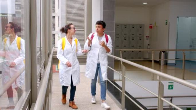 拉丁美洲开朗的医学院学生在大学的走廊里走来走去，背着背包，一边说话一边穿着实验服