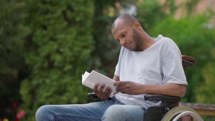 在夏日，全神贯注地坐在轮椅上的非洲裔美国残疾人读者在户外欣赏文学作品。集中男子阅读书籍的中等镜头肖像