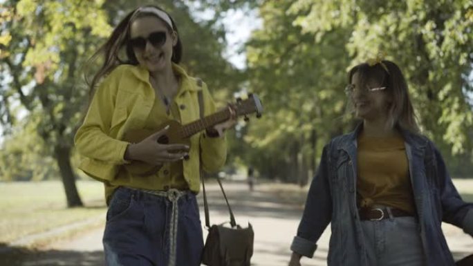 两个戴着墨镜的轻松快乐的女嬉皮士在阳光下户外行走，演奏夏威夷四弦琴和唱歌的肖像。在20世纪60年代享
